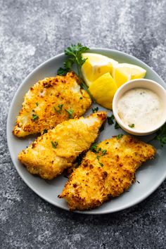 chicken schnitz on a plate with lemon wedges and parmesan sauce