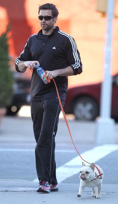 a man walking his dog down the street while holding onto a water bottle and wearing sunglasses