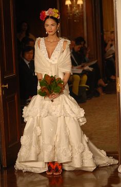 a woman in a wedding dress with flowers on her head walking down the runway at a fashion show