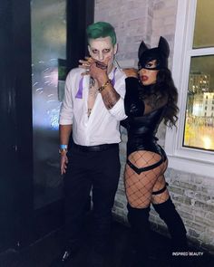 a man and woman dressed up as batman and catwoman posing for the camera in front of a brick building