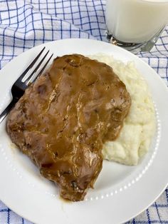 a white plate topped with meat and mashed potatoes next to a glass of milk