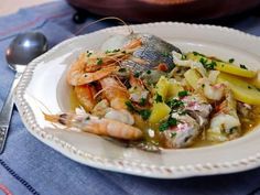 a white plate topped with shrimp and potatoes on top of a blue table cloth next to a bowl of soup