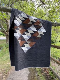 a black quilt hanging from a tree in the grass near a fence and some trees