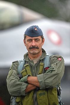 a man with a mustache and uniform standing in front of a car on the street