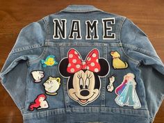 a denim jacket with mickey mouse and other disney characters on the back, sitting on a wooden floor