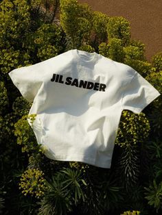 a white t - shirt with the word jil sander on it laying in some bushes