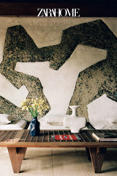 a coffee table with vases and flowers on it in front of a wall painting