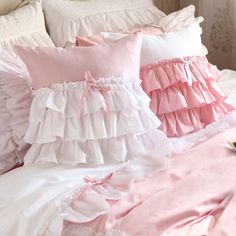 pink and white pillows on a bed with ruffles around the edges, along with a bouquet of flowers