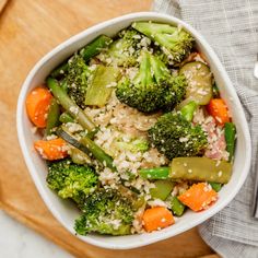 a bowl filled with rice, broccoli and carrots on top of a wooden cutting board