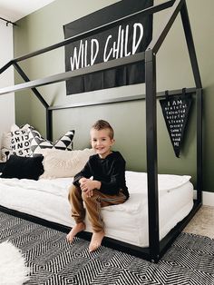 a young boy sitting on top of a bed in a room with black and white decor