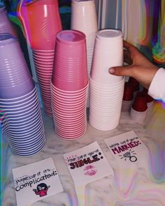 there are many different colored cups on the table and one is pointing at them with a finger