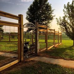 a wooden fence with metal gate in grassy area next to trees and grass field at sunset