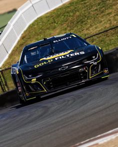 a black and yellow car driving on a race track with grass in the back ground