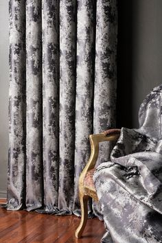 a chair sitting in front of a window covered in gray velvet curtains and drapes