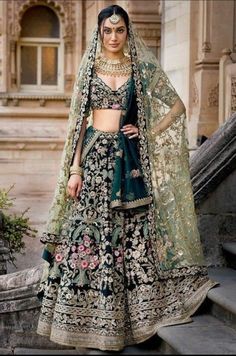 a woman in a black and green lehenga is standing on steps with her hand on her hip