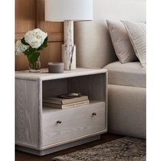 a table with a lamp and flowers on it in front of a couches headboard