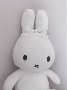 a white stuffed rabbit with a bow on its head sitting against a wall in a corner