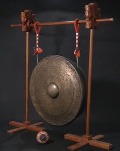 two gongs on wooden stands with decorations hanging from the top and one holding an object