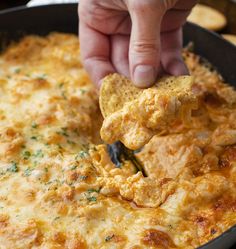 a hand holding a tortilla chip over a skillet filled with cheesy cheese