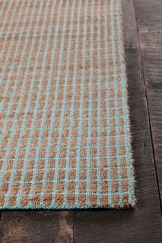 a brown and blue checkered rug on top of a wooden floor next to a window