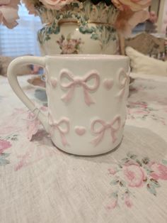 a white cup with pink bows on it sitting next to a vase filled with flowers