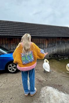 a woman standing in front of a flock of birds next to a building with a sign on it