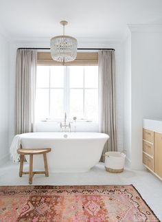 a white bath tub sitting under a window next to a wooden stool on top of a rug