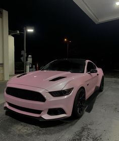 a pink car parked in front of a gas station with its hood up at night