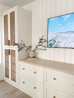 a television mounted on the wall above a dresser with drawers and vases in front of it