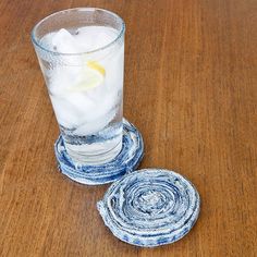 two glass coasters sitting on top of a wooden table next to a cup filled with ice