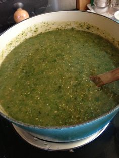 a pot filled with green soup sitting on top of a stove next to a wooden spoon