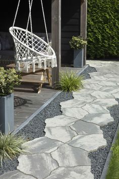 a white hammock hanging from a wooden structure next to a stone walkway and potted plants