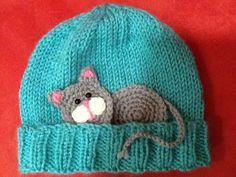 a knitted hat with a small gray rat on it's side, sitting on top of a red surface