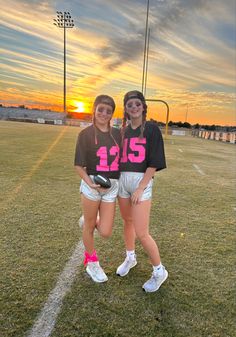 two girls standing on a football field with the sun setting in the sky behind them