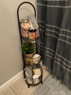 three tiered metal basket with plants in it next to a towel rack and shower curtain