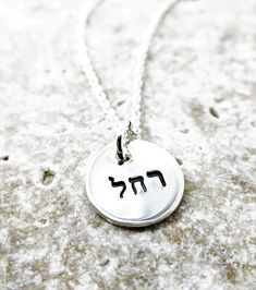 "This petite pendant necklace is just lovely! Hand stamped with your choice of name (example: Rachel) in Hebrew, this 1/2\" pendant necklace would make the perfect Bat Mitzvah, birthday, Hanukkah or anytime gift! Necklace will arrive with your choice of a 16\", 18\" or 20\" double rope cable chain. Please specify the following in the \"notes to seller\" at purchase: 1. Name you would like stamped Necklace suitable for 3-5 letters across, 5-10 letters around the outer edge. If you are unsure of h Meaningful Round Pendant Nickel-free Charm Necklace, Hand Stamped Round Pendant Charm Necklace, Silver Charm Necklace With Custom Name And Round Pendant, Silver Charm Necklace With Custom Name On Round Pendant, Custom Name Silver Charm Necklace With Round Pendant, Silver Custom Name Charm Necklace With Round Pendant, Silver Name Necklace With Charms, Silver Name Necklace With Charms And Round Pendant, Silver Name Necklace With Round Pendant And Charms