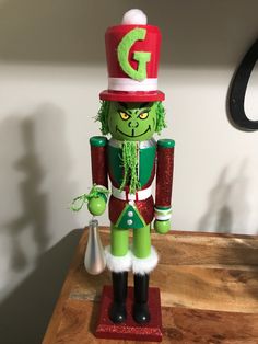 a green and red nutcracker on top of a wooden table next to a lamp