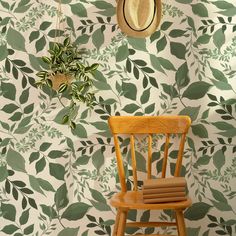 a wooden chair sitting in front of a wall with green leaves on it and a straw hat hanging from the back