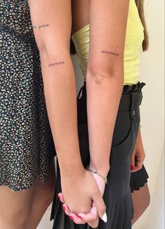 two women holding hands with tattoos on their arms and the words together are written in cursive writing