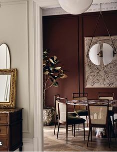 a dining room with red walls and white trim on the wall, an oval mirror hanging from the ceiling