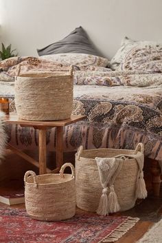 three baskets on the floor in front of a bed with a rug and pillows behind it