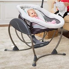 a woman sitting on a couch with a baby in a bouncer next to her