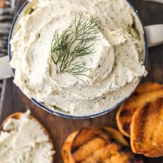 a bowl filled with mashed potatoes on top of a wooden cutting board next to sliced bread