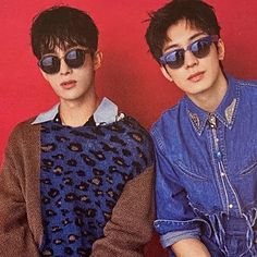 two young men sitting next to each other in front of a red wall wearing sunglasses