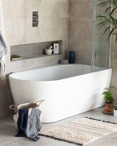 a white bath tub sitting on top of a bathroom floor next to a potted plant