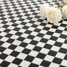 three white roses sitting on top of a black and white checkered floor