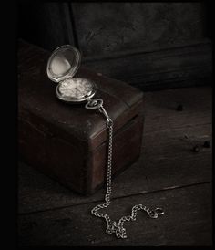 an open pocket watch sitting on top of a wooden box next to a chain necklace