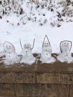 four snowmen standing in the middle of a brick wall with sticks sticking out of them