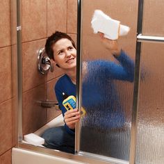 a woman sitting in a shower holding a spray bottle