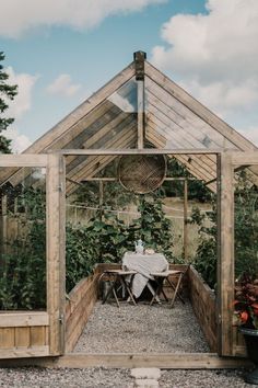 a small wooden greenhouse with tables and chairs in the center, surrounded by greenery